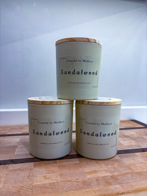 Three Sandalwood beeswax candles by Created by Madison stacked on a wooden surface