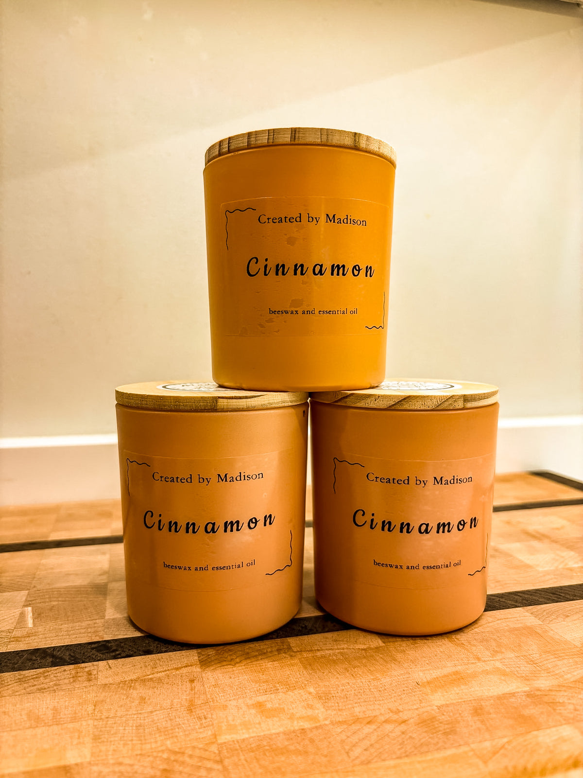 Three Cinnamon beeswax candles by Created by Madison stacked in a pyramid on a wood surface